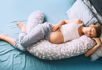 Pregnant woman in bed sleeping on her side with support pillow between her legs and under her belly