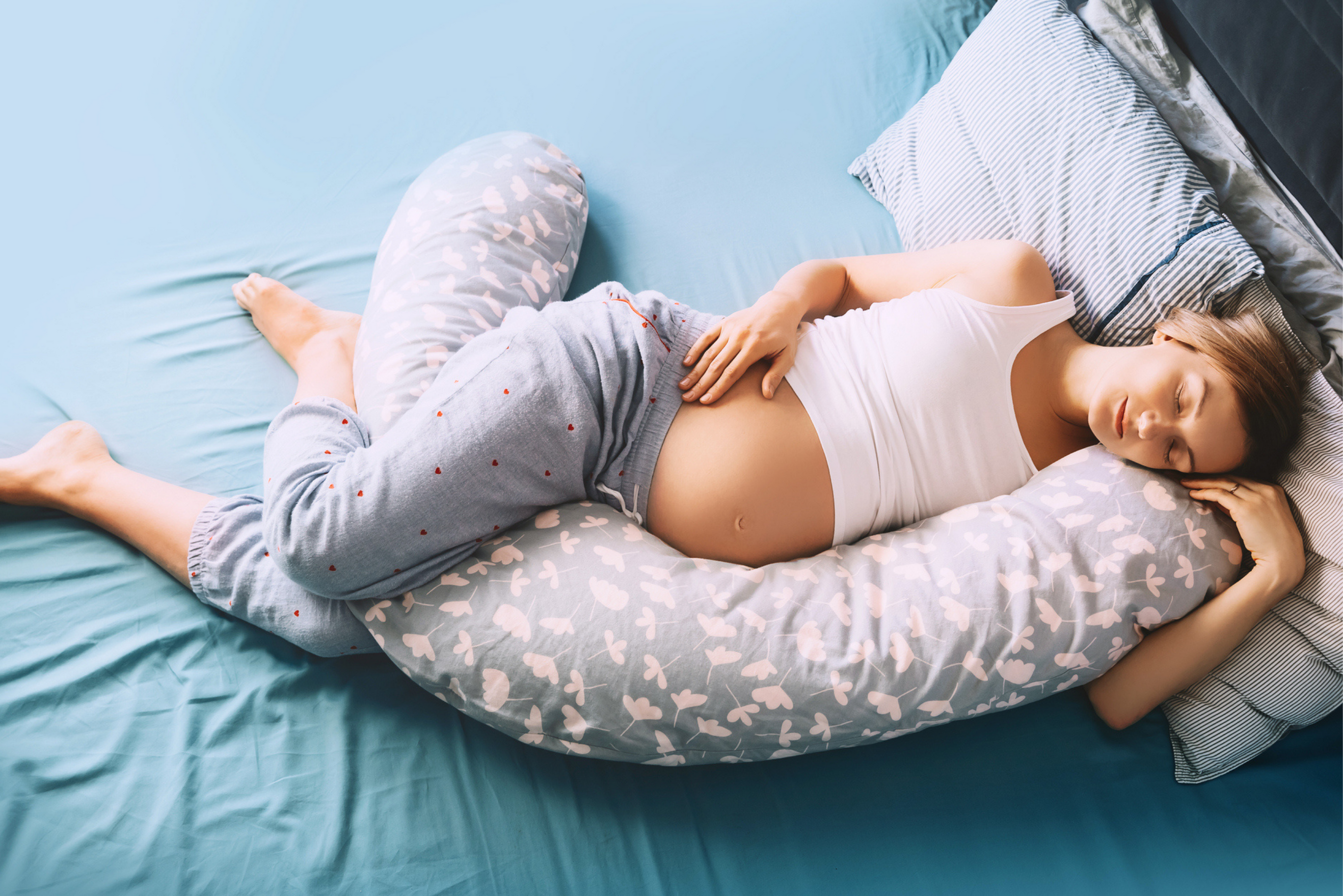 Pregnant woman in bed sleeping on her side with support pillow between her legs and under her belly